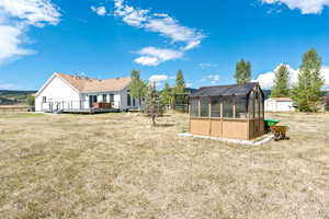 Rear view of property featuring a greenhouse, an outdoor structure, a deck, and a lawn