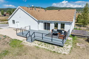 Back of property featuring a deck with mountain view, stucco siding, an outdoor living space with a fire pit, and roof with shingles