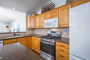 Kitchen featuring white appliances, a sink, vaulted ceiling, decorative backsplash, and a textured ceiling