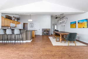 Dining room featuring high vaulted ceiling, wood finished floors, a ceiling fan, baseboards, and a fireplace
