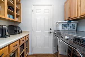 Laundry room featuring independent washer and dryer, cabinet space, and dark wood-style flooring