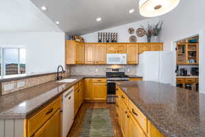 Kitchen with white appliances, a sink, vaulted ceiling, backsplash, and a textured ceiling