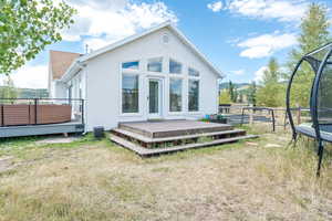 Rear view of house featuring a deck with mountain view, a trampoline, and stucco siding