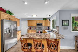 Kitchen with stainless steel appliances, a sink, a peninsula, decorative backsplash, and light wood-type flooring