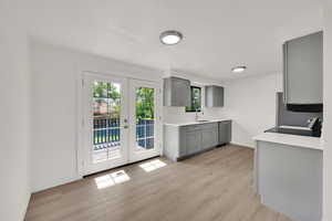 Kitchen with gray cabinetry, stainless steel dishwasher, light wood-type flooring, and light countertops