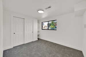 Unfurnished bedroom with dark carpet, a textured ceiling, and a closet