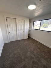 Unfurnished bedroom with a textured ceiling, baseboards, a closet, and dark carpet