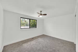 Carpeted spare room featuring ceiling fan and baseboards