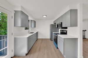 Kitchen with stainless steel appliances, gray cabinetry, and light wood-type flooring