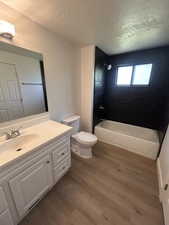 Full bath featuring a textured ceiling, vanity, wood finished floors, toilet, and  shower combination