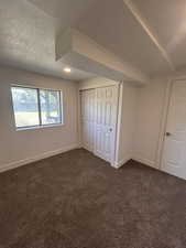 Unfurnished bedroom with dark colored carpet, baseboards, a closet, and a textured ceiling