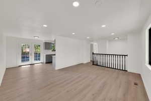 Unfurnished living room featuring recessed lighting, light wood finished floors, and french doors
