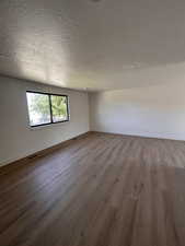 Unfurnished room featuring a textured ceiling, wood finished floors, and baseboards