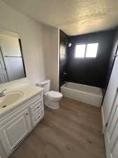 Full bathroom with toilet, vanity, wood finished floors, bathtub / shower combination, and a textured ceiling