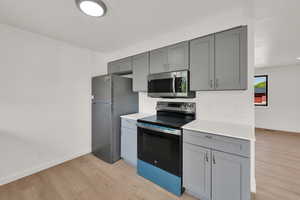 Kitchen with appliances with stainless steel finishes, gray cabinets, light wood finished floors, and light countertops