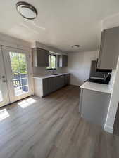 Kitchen with light wood-style flooring, gray cabinetry, light countertops, baseboards, and stainless steel dishwasher