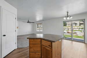 Kitchen featuring dark countertops, a chandelier, ceiling fan, a kitchen island, and pendant lighting
