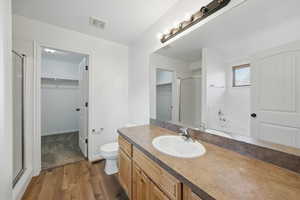 Full bathroom featuring a shower stall, a walk in closet, vanity, and wood finished floors