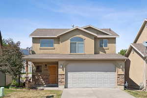 View of front of home featuring concrete driveway, stone siding, an attached garage, and stucco siding