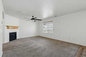 Unfurnished living room featuring a ceiling fan, a glass covered fireplace, baseboards, and carpet floors