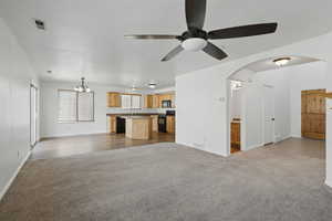 Unfurnished living room featuring carpet floors, arched walkways, a chandelier, a ceiling fan, and baseboards