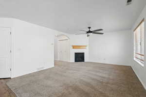 Unfurnished living room featuring a ceiling fan, arched walkways, a glass covered fireplace, baseboards, and carpet floors