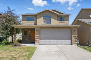 View of front of house featuring stone siding, stucco siding, concrete driveway, a garage, and a front lawn
