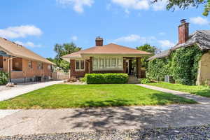 Bungalow featuring a front lawn, brick siding, a chimney, and central AC unit