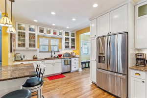 Kitchen with appliances with stainless steel finishes, a sink, recessed lighting, light wood finished floors, and decorative backsplash