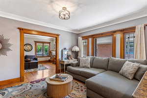 Living room with baseboards, wood finished floors, ornamental molding, and a chandelier