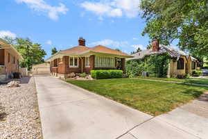 View of front of property with an outdoor structure, brick siding, a front lawn, a chimney, and central AC