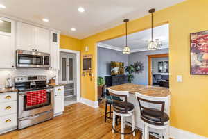 Kitchen featuring stainless steel appliances, baseboards, light wood-style floors, white cabinets, and decorative backsplash