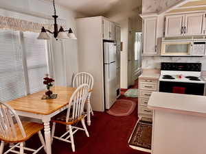 Kitchen featuring white appliances, a chandelier, light countertops, and hanging light fixtures