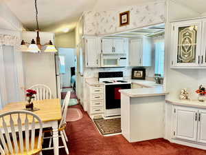 Kitchen with white appliances, dark colored carpet, light countertops, a sink, and a peninsula