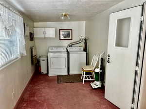 Washroom featuring carpet, washer and clothes dryer, a textured ceiling, cabinet space, and baseboards