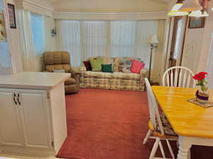Living area featuring light colored carpet, lofted ceiling, and crown molding