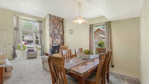 Dining room featuring light colored carpet, baseboards, a stone fireplace, and lofted ceiling