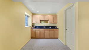 Kitchen featuring dark countertops, light carpet, baseboards, recessed lighting, and a sink