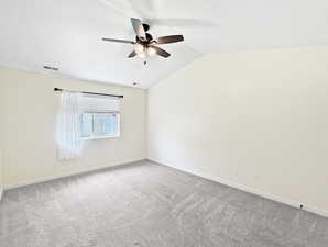 Carpeted spare room featuring ceiling fan, vaulted ceiling, and baseboards