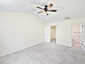 Unfurnished bedroom featuring carpet flooring, a spacious closet, vaulted ceiling, baseboards, and ensuite bathroom