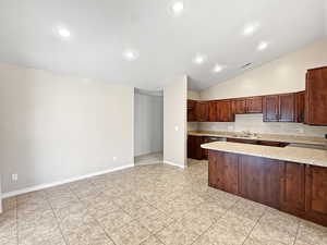 Kitchen with a sink, light stone countertops, light tile patterned flooring, lofted ceiling, and a peninsula