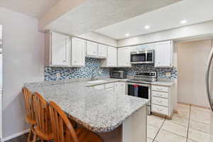 Kitchen featuring appliances with stainless steel finishes, a sink, a peninsula, a kitchen breakfast bar, and white cabinets
