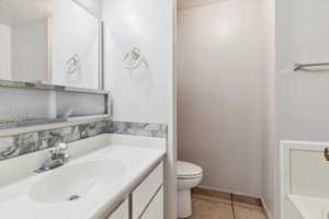 Bathroom featuring toilet, tile patterned floors, vanity, a textured ceiling, and baseboards