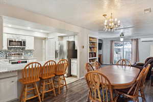 Dining space featuring a wall mounted AC, a textured ceiling, a ceiling fan, light wood finished floors, and a chandelier