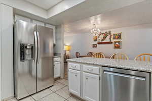 Kitchen featuring appliances with stainless steel finishes, a textured ceiling, white cabinetry, light tile patterned flooring, and a chandelier