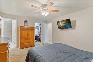 Bedroom featuring a spacious closet, light carpet, a textured ceiling, ceiling fan, and ensuite bathroom