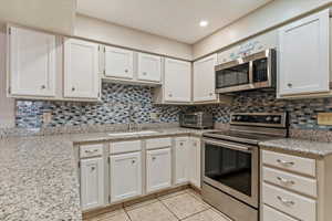Kitchen featuring stainless steel appliances, backsplash, light tile patterned floors, white cabinetry, and recessed lighting