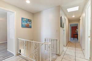 Hallway with light tile patterned floors, an upstairs landing, a textured ceiling, and recessed lighting