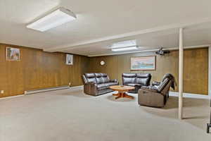 Carpeted living room featuring baseboard heating, beam ceiling, a textured ceiling, and wood walls