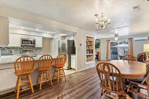 Dining space featuring ceiling fan, dark wood-style floors, a textured ceiling, built in shelves, and a chandelier